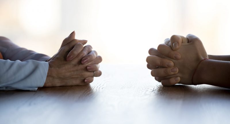 Two people sitting across from each other with their hands folded