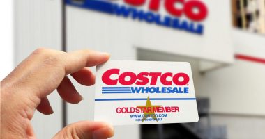 A Costco Gold Membership card held in front of a Costco warehouse entrance