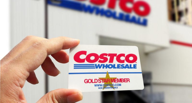 A Costco Gold Membership card held in front of a Costco warehouse entrance