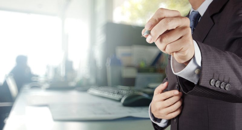 Businessman holding a pen in front of people surrounded at a table in a boardroom.