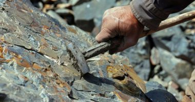 A worker using a pickaxe to extract uranium ore from a rock face.