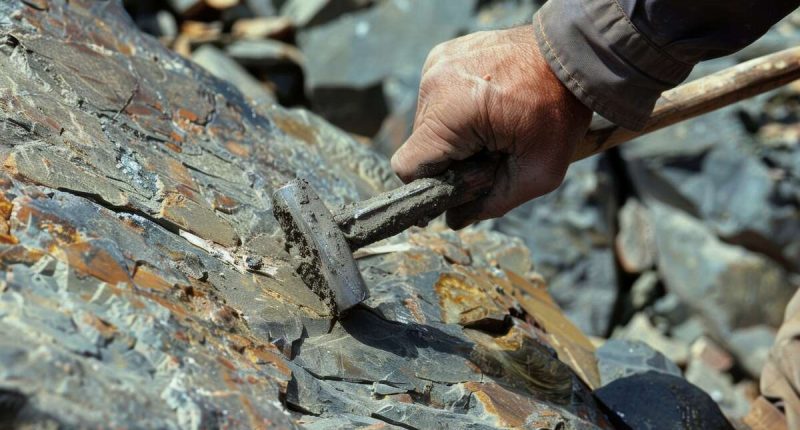 A worker using a pickaxe to extract uranium ore from a rock face.