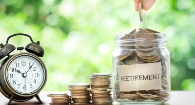 Hand putting Coins in glass jar with retro alarm clock, retirement