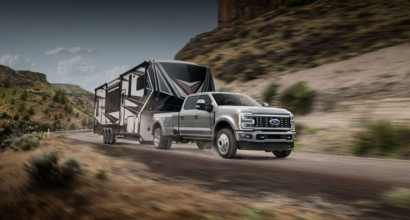 A Ford F-Series Super Duty pickup truck with a trailer driving on a desert road.