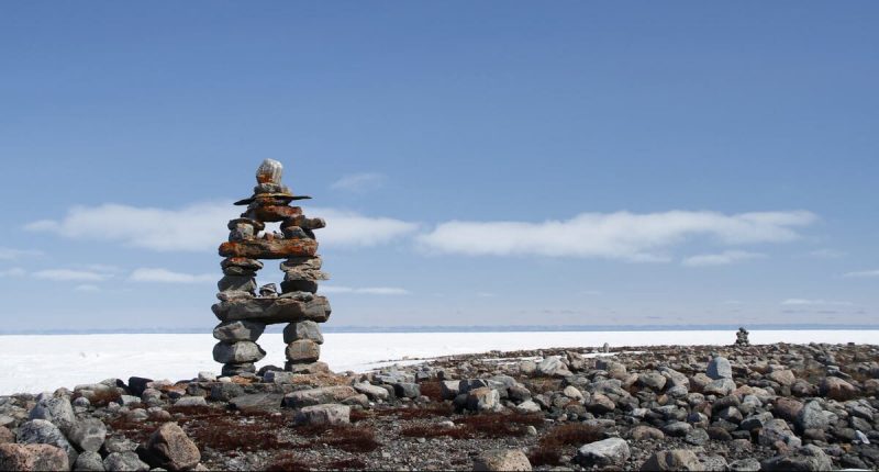 Inuksuk landmark with frozen bay in the background near Arviat, Nunavut