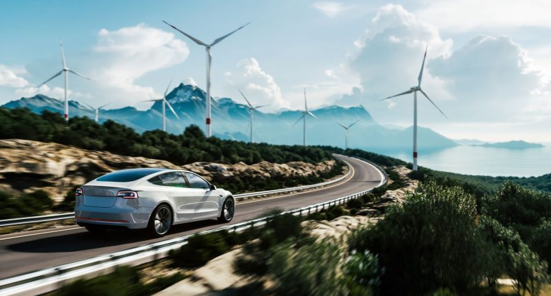 Electric car drives on a highway with wind turbines in background.